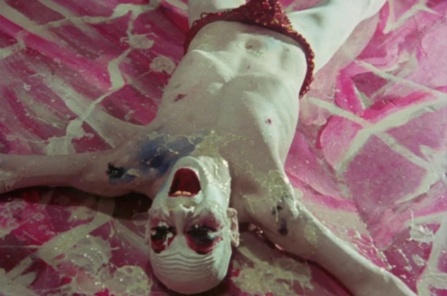 Sebastiane (1976) movie still: medium — A person lies on a pink surface covered with white viscous fluid. The subject wears white face paint and a…