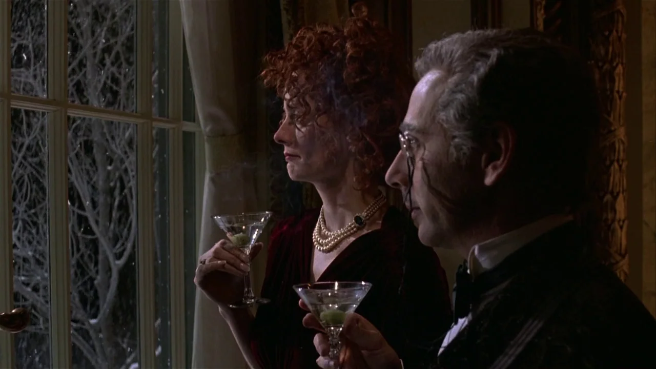 Batman Returns (1992) movie still: medium — A dark, elegant room with a large window looking out onto a snowy night. A woman in a red velvet dress…