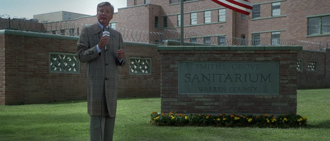Halloween (2007) movie still: fullbody — A brick wall with barbed wire surrounds a large medical facility building in daylight. A news reporter…
