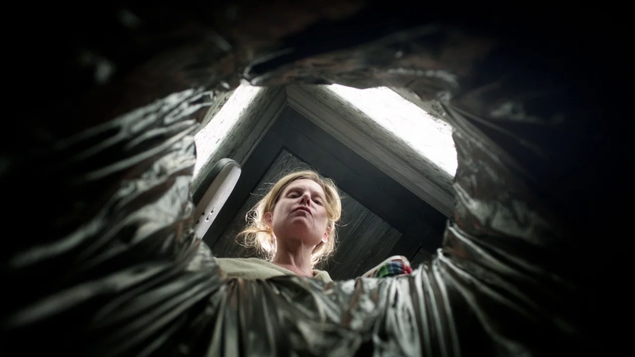 Curse of Chucky (2013) movie still: closeup — A woman stares down into a dark, metallic cylindrical container from a high angle. The viewer sees her…
