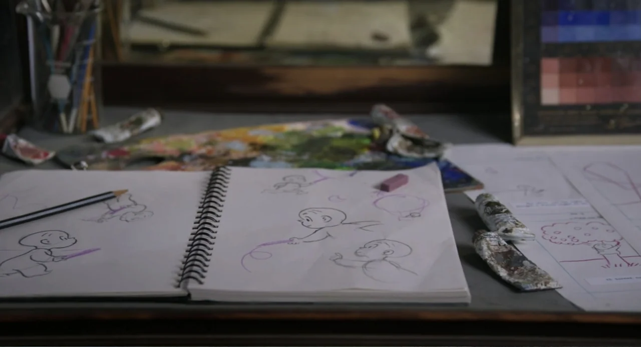 Harold and the Purple Crayon (2024) movie still: closeup — An artist desk surface holds an open sketchbook containing pencil drawings of cartoon…