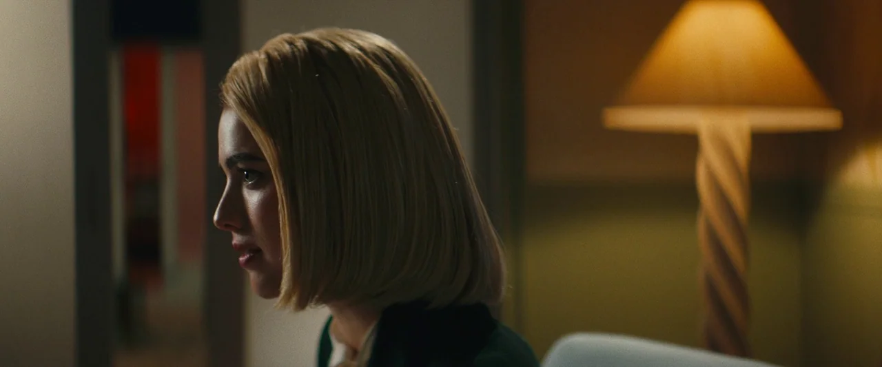 Sanctuary (2023) movie still: closeup — A dimly lit room contains a person in a dark blazer beside a lamp. The subject looks toward the side of the…