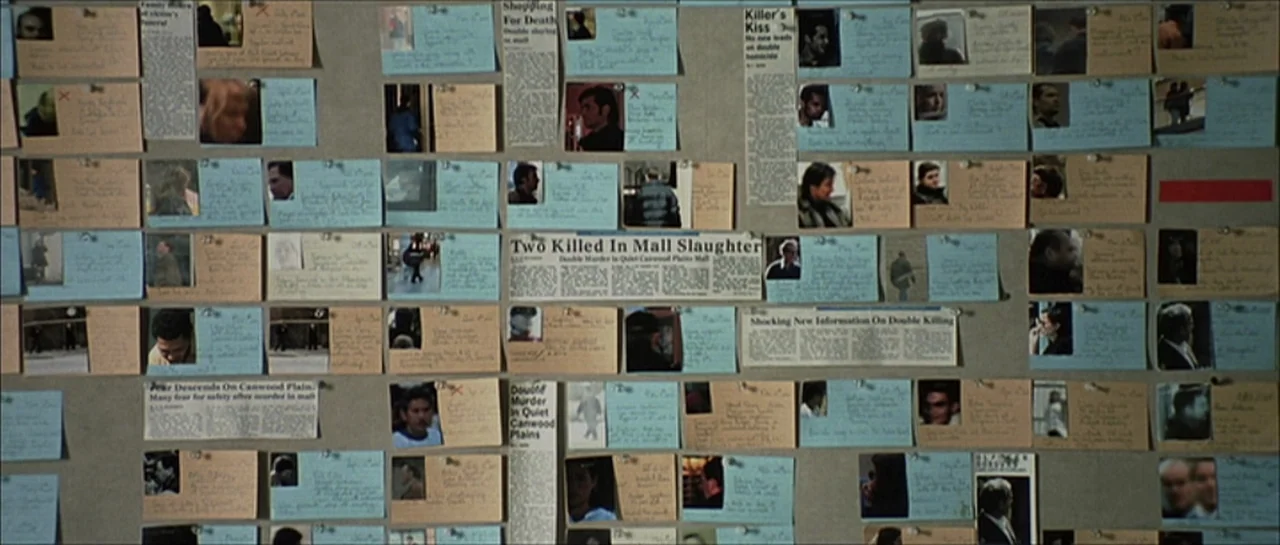 Fear X (2003) movie still: wide — A wall covered in numerous paper notes, newspaper clippings, and small photographs pinned up. The documents are…