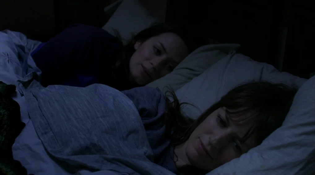 Your Sister’s Sister (2011) movie still: medium — A dimly lit room with two women lying next to each other in bed. The women are covered by sheets…