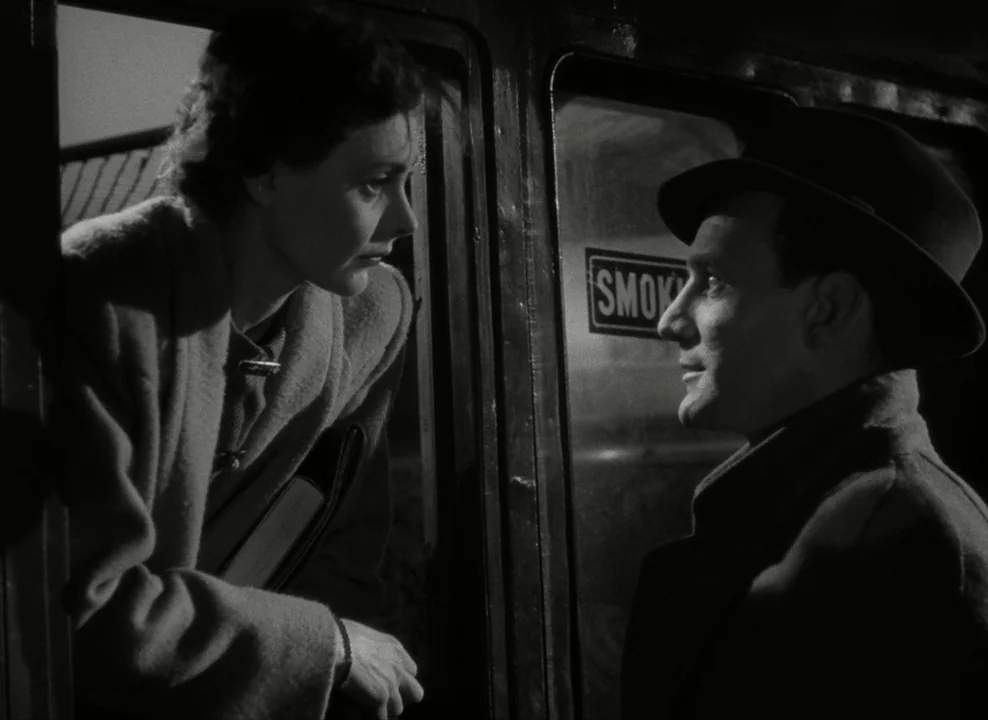 Brief Encounter (1945) movie still: medium — The interior of a 1940s passenger train at night featuring a smoking carriage sign. A man stands in the…