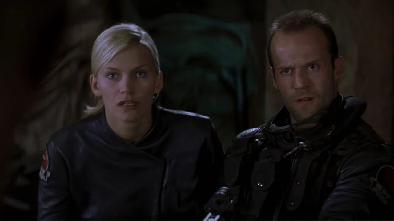 Ghosts of Mars (2001) movie still: medium — A dark indoor space where two individuals appear to be waiting in shadows. A man and a woman look…