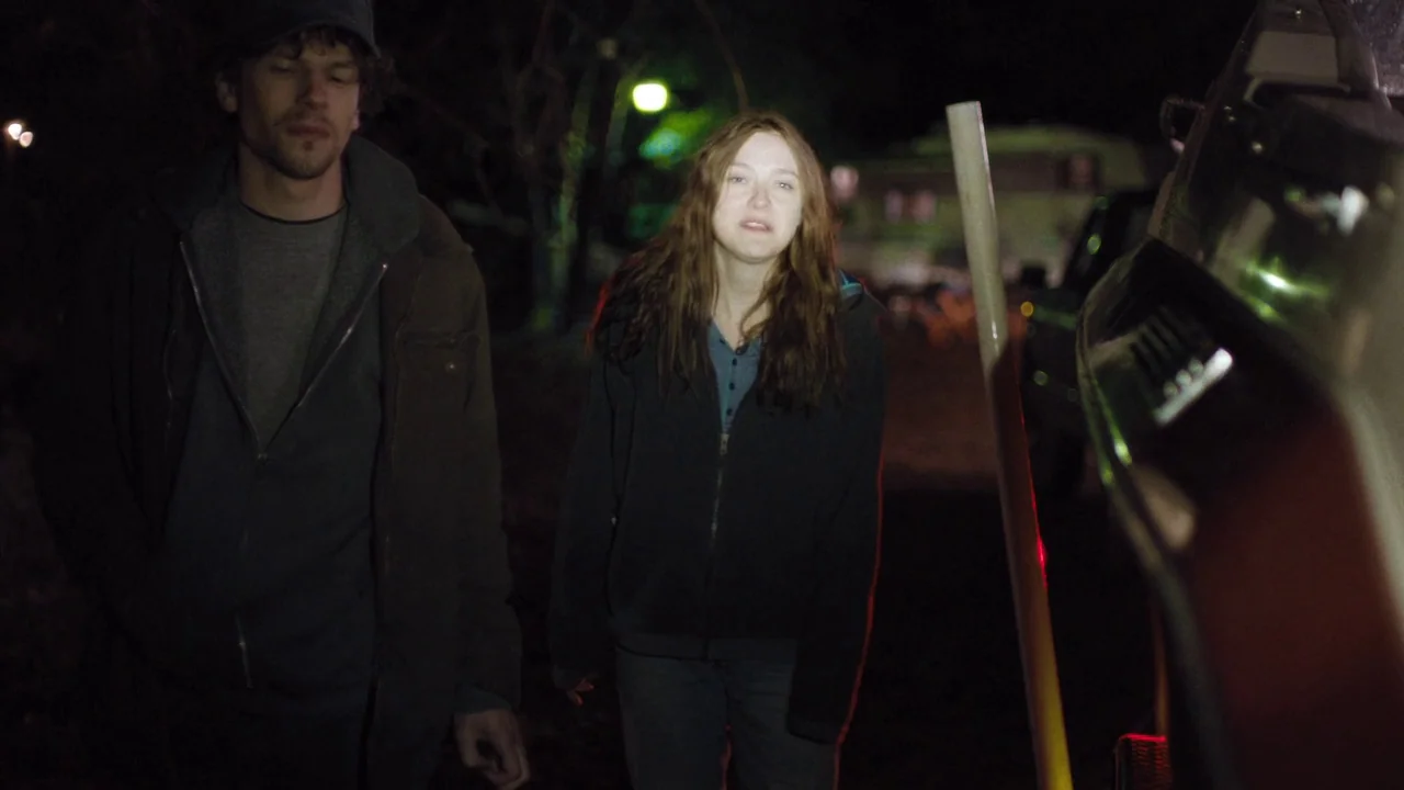 Night Moves (2013) movie still: medium — Two individuals stand in a dark, rural exterior location at night. The man stands to the left while the…
