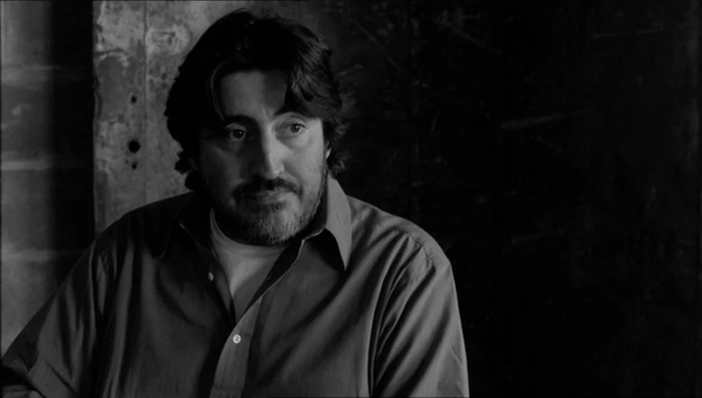 Coffee and Cigarettes (2003) movie still: medium — A man stands against a dark, textured wall in a dimly lit space. He is looking off to the side…