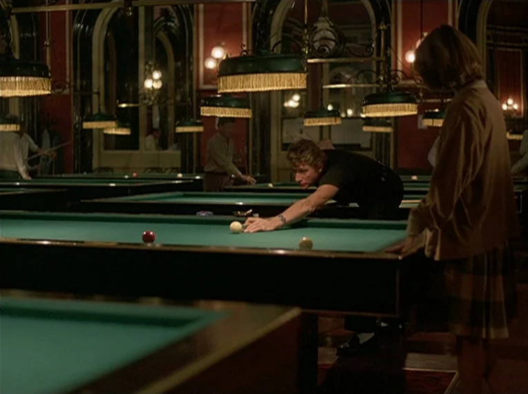 Detective (1985) movie still: medium — An indoor billiard hall features several green tables lit by hanging lamps in a dark room. A man leans over…