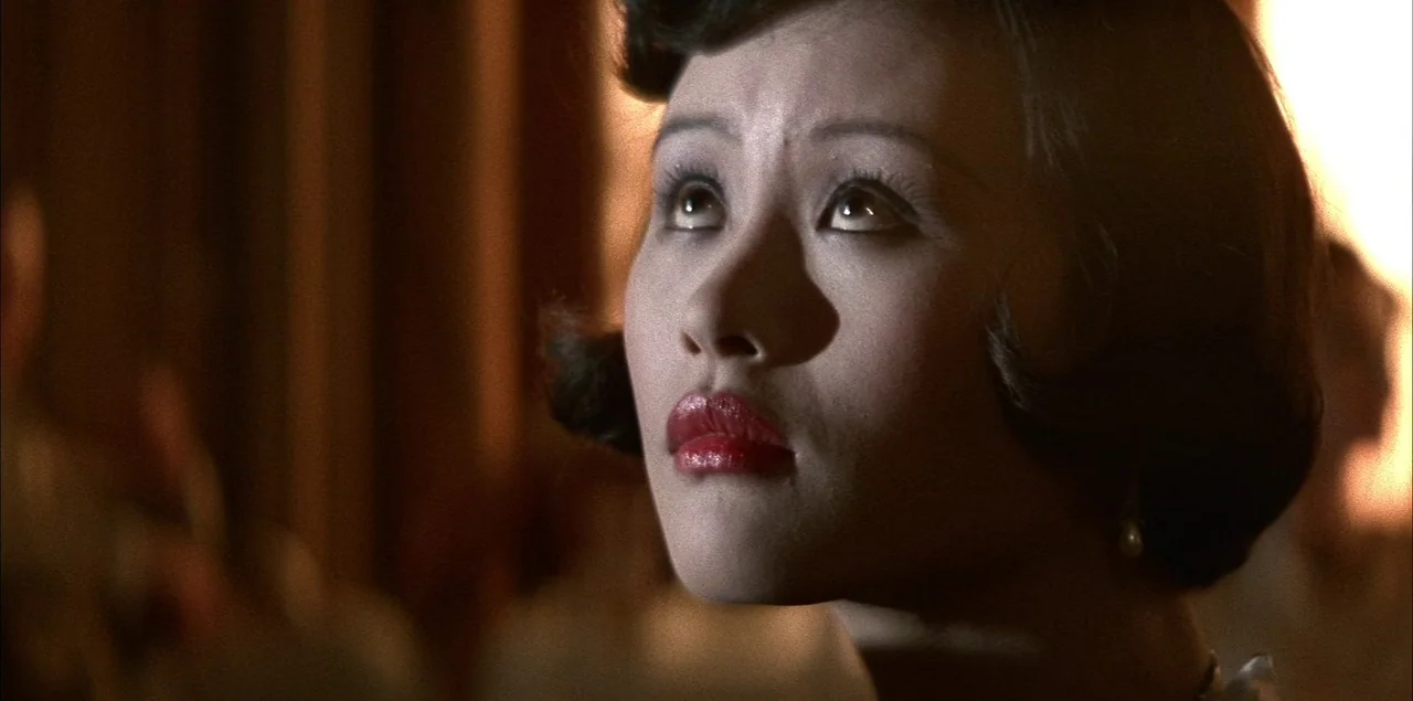 The Last Emperor (1987) movie still: closeup — A dimly lit room with dark paneling creates an atmospheric setting for the woman. She tilts her head…