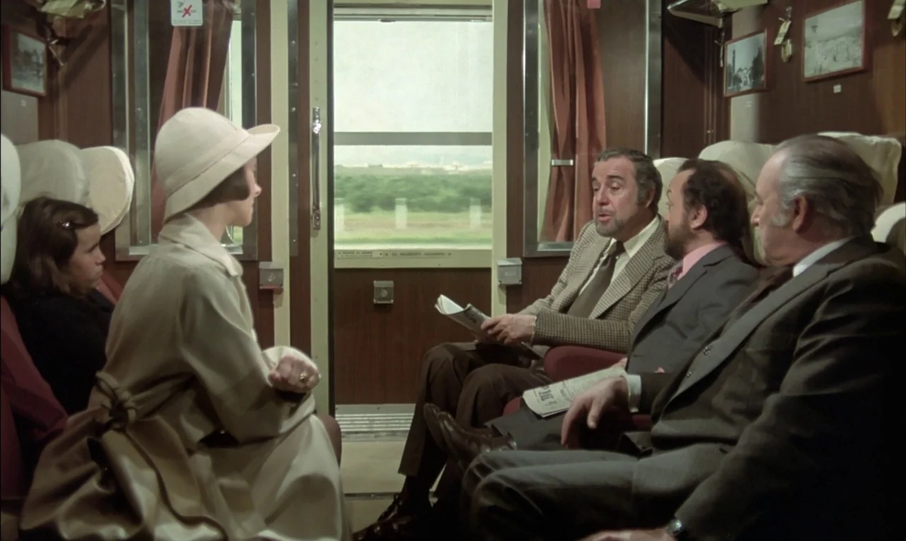 That Obscure Object of Desire (1977) movie still: medium — A vintage passenger train compartment features wood paneling and red curtains by the…