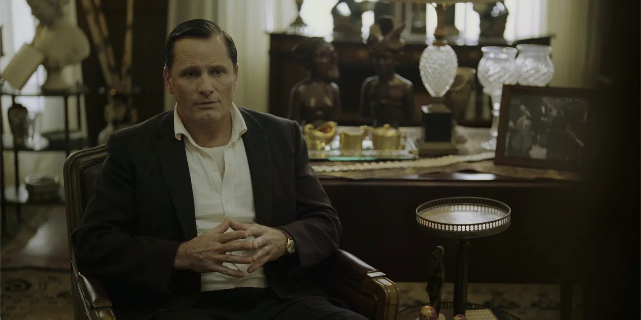 Green Book (2018) movie still: medium — A study filled with ornate wooden furniture, statues, and various antique decorative objects. A man in a…