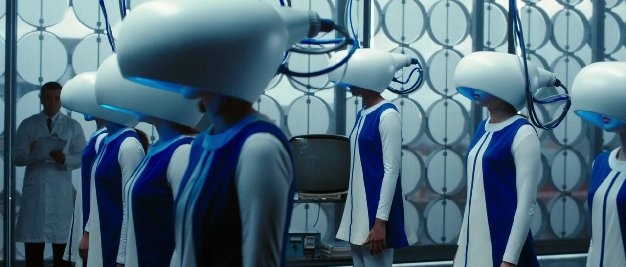 Predestination (2014) movie still: medium — A clinical room features a repeating circular wall pattern behind multiple women in helmets. A man in a…