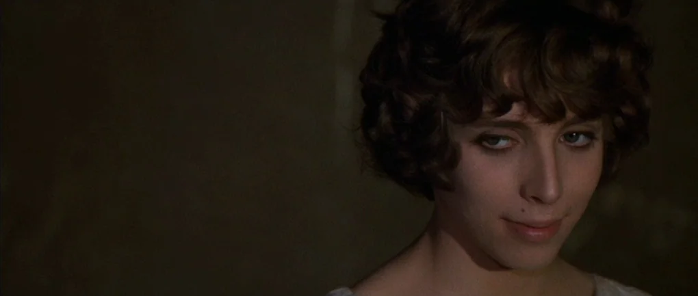 Fellini – Satyricon (1969) movie still: closeup — A close-up shot focuses on a young woman's face against a dark, featureless background. She wears…