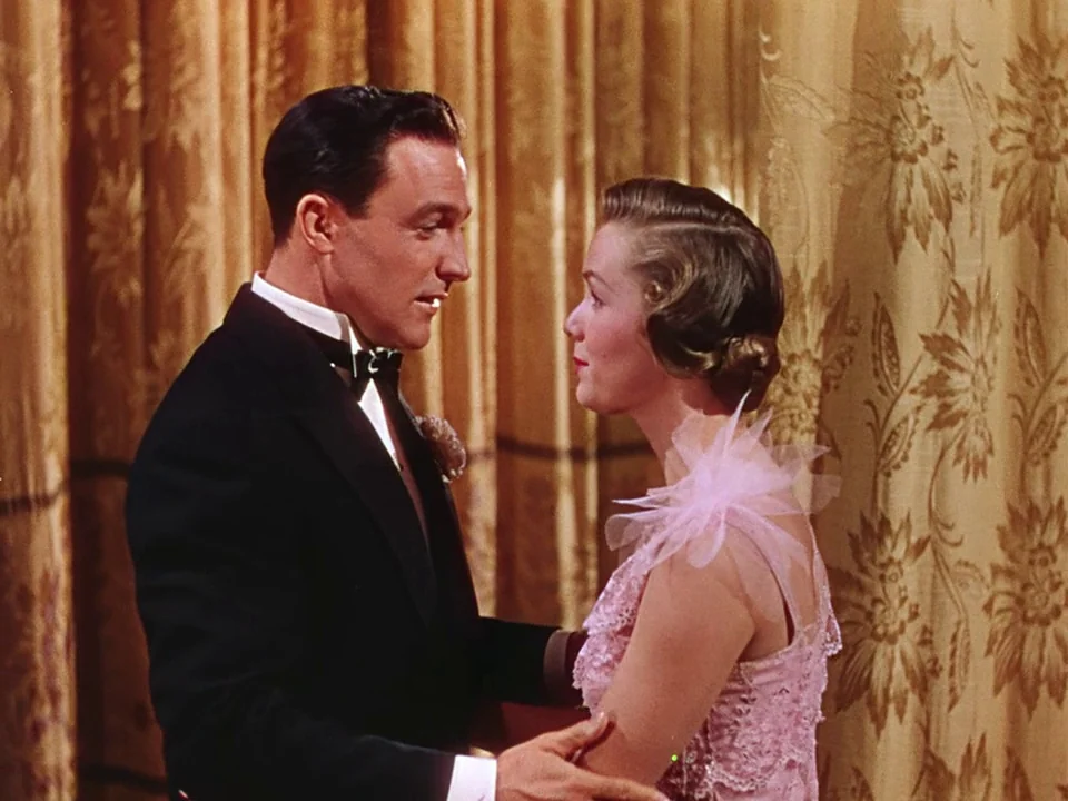 Singin’ in the Rain (1952) movie still: medium — A formal indoor setting features heavy gold-patterned floor-to-ceiling curtains in the background.…