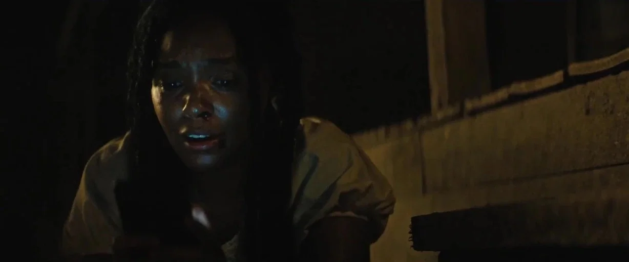 Antebellum (2020) movie still: closeup — A dark outdoor space at night shows the corner of a wooden structural element. A young woman looks downward…