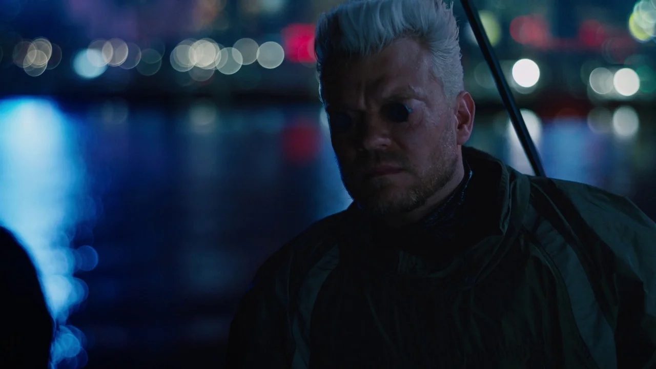 Ghost in the Shell (2017) movie still: closeup — A man with stark white hair stands at night near a dark body of water. The blurred city lights…