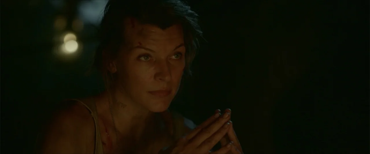 Monster Hunter (2020) movie still: closeup — A dark outdoor space illuminated by a nearby firelight source. A woman with minor injuries on her face…