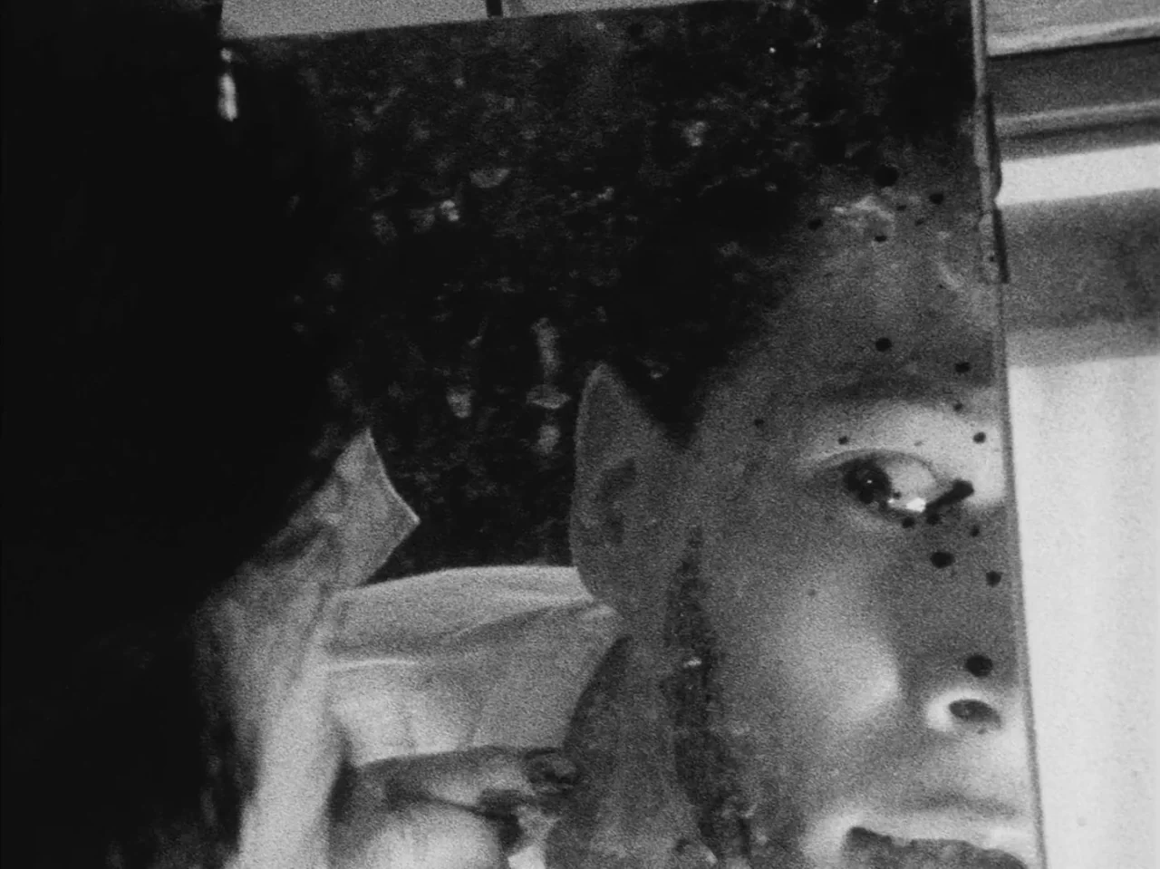 Tetsuo: The Iron Man (1989) movie still: closeup — A person looks into a reflective surface in a dimly lit environment. The tight framing captures…