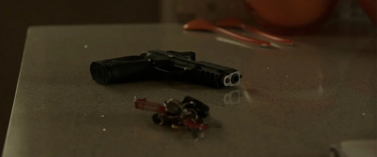 Den of Thieves (2018) movie still: closeup — A dark stone countertop holds a black semi-automatic pistol and a set of keys. The objects lie…