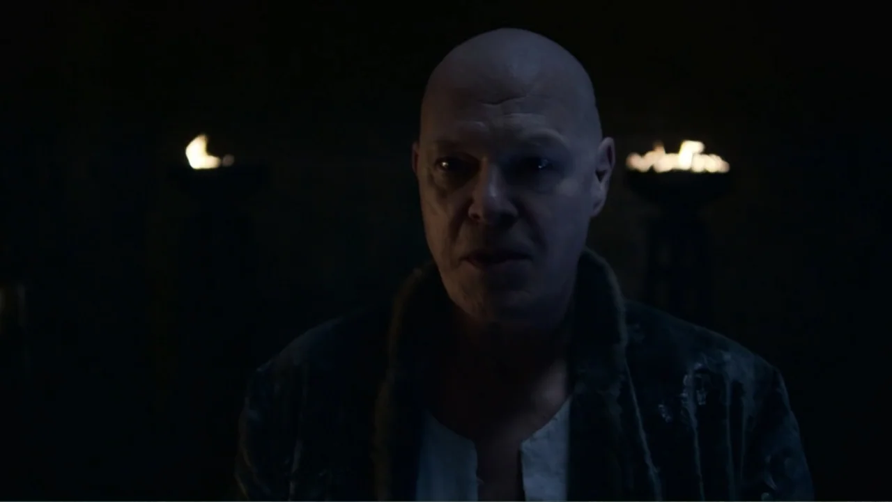 Underworld: Blood Wars (2016) movie still: closeup — A dark, dimly lit stone chamber with flickering torches visible in the background. A bald man…