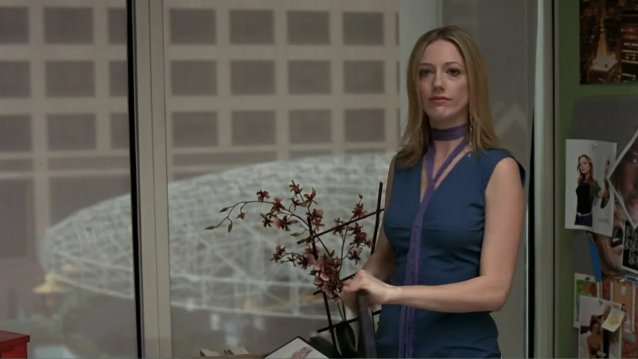 13 Going on 30 (2004) movie still: medium — An office interior features a large glass window overlooking a building structure outside. A woman in a…