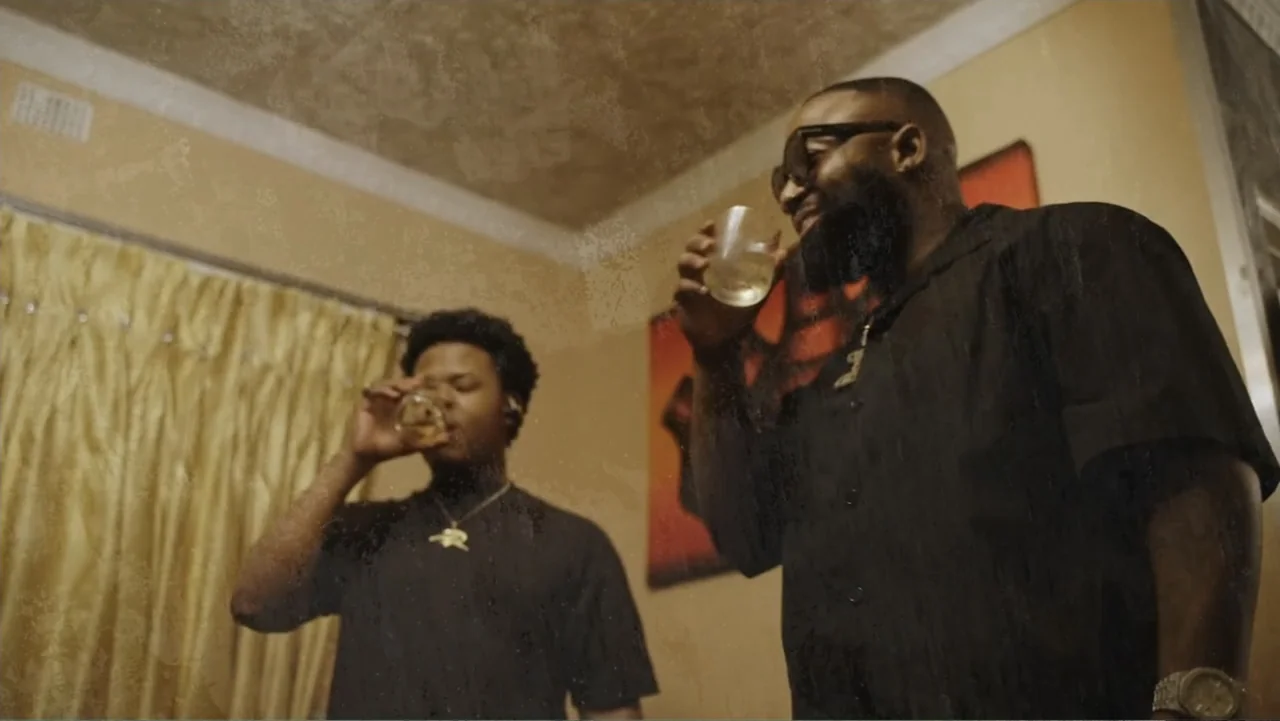 African Throne World Tour (2024) movie still: medium — A residential interior space featuring tan curtains and beige walls. Two men in dark clothing…