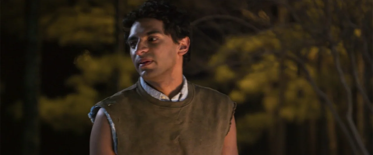 Office Uprising (2018) movie still: medium — A man stands in an outdoor area at night with dark trees in background. The man looks toward the left…
