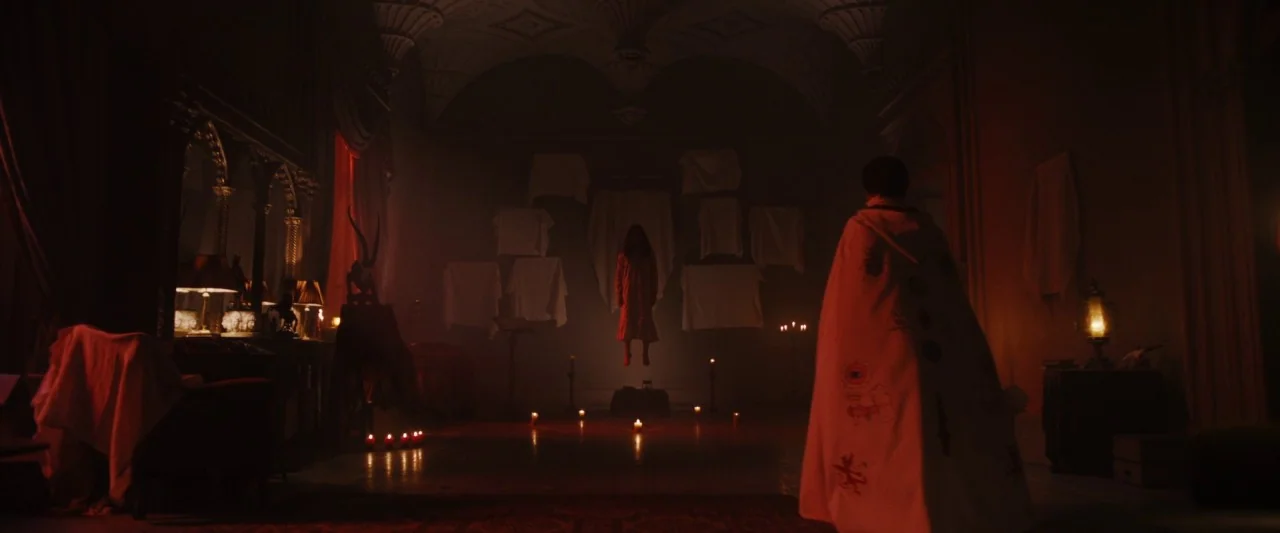 Extra Ordinary (2019) movie still: wide — A dark, candlelit room features multiple white cloths draped on the back wall. A figure in a…