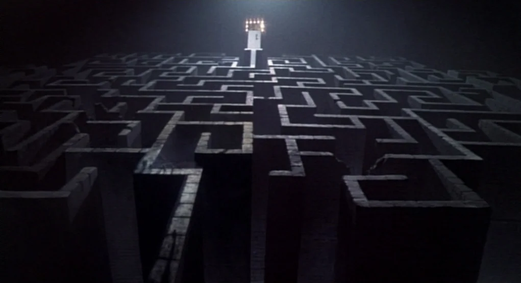 Time Bandits (1981) movie still: establishing — A dense outdoor stone hedge maze stands under the dark cover of night. A lone glowing light sits…