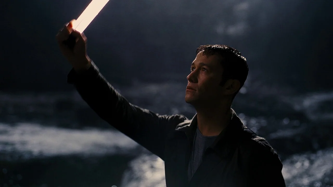The Dark Knight Rises (2012) movie still: medium — A dark, rocky cave interior is illuminated only by a small, bright handheld light. A man in a…