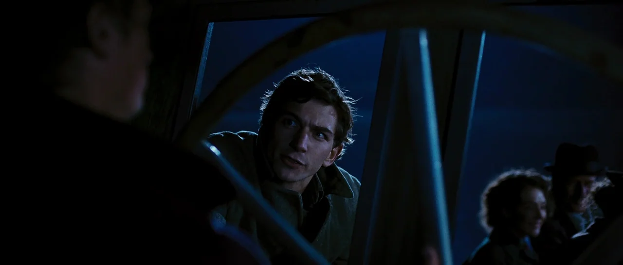 Black Book (2006) movie still: medium — A man in a coat stands on a dark boat deck at night. He is illuminated by blue moonlight while observing…