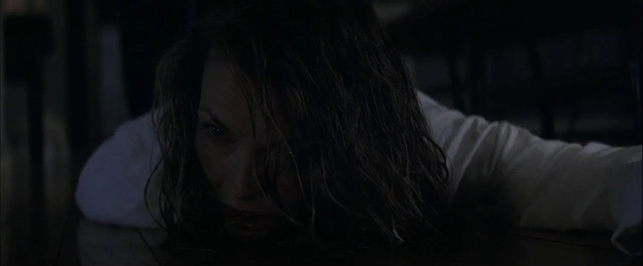 What Lies Beneath (2000) movie still: closeup — A dark, dimly lit room with a woman lying flat on a wooden surface. The subject is oriented at a low…