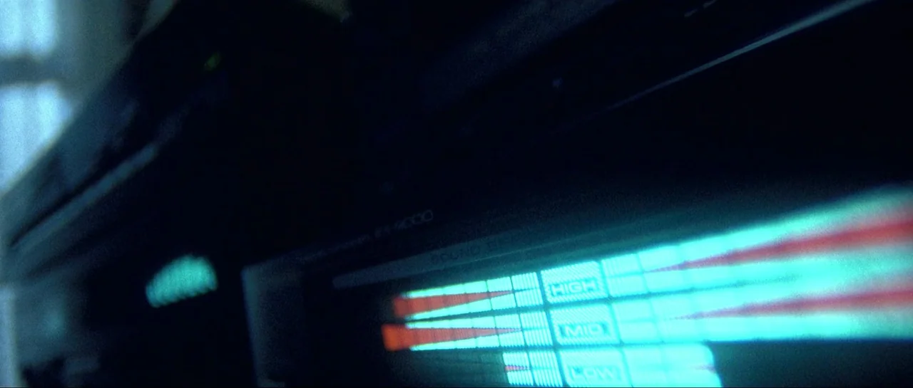 Opera (1987) movie still: closeup — A close-up of a dark vintage audio equalizer unit sitting in a dim room. The digital display glows with bright…