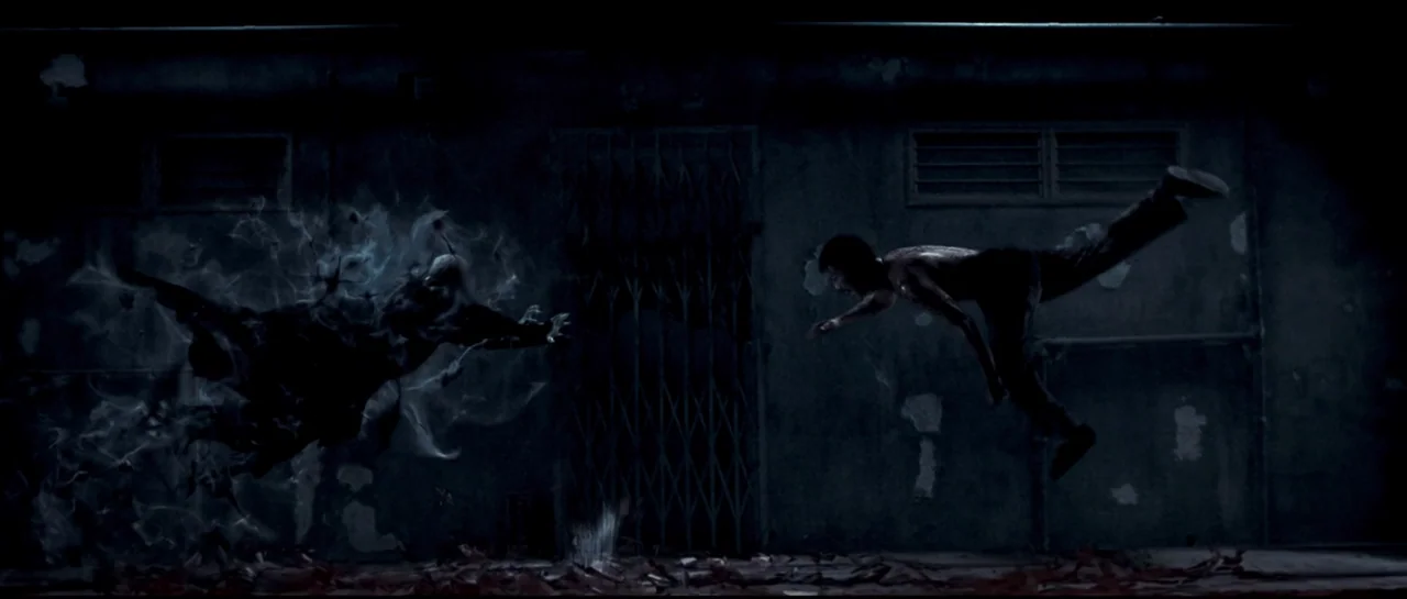 Rigor Mortis (2013) movie still: wide — A dark outdoor alleyway features a weathered wall and a locked metal security gate. A man lunges mid-air…