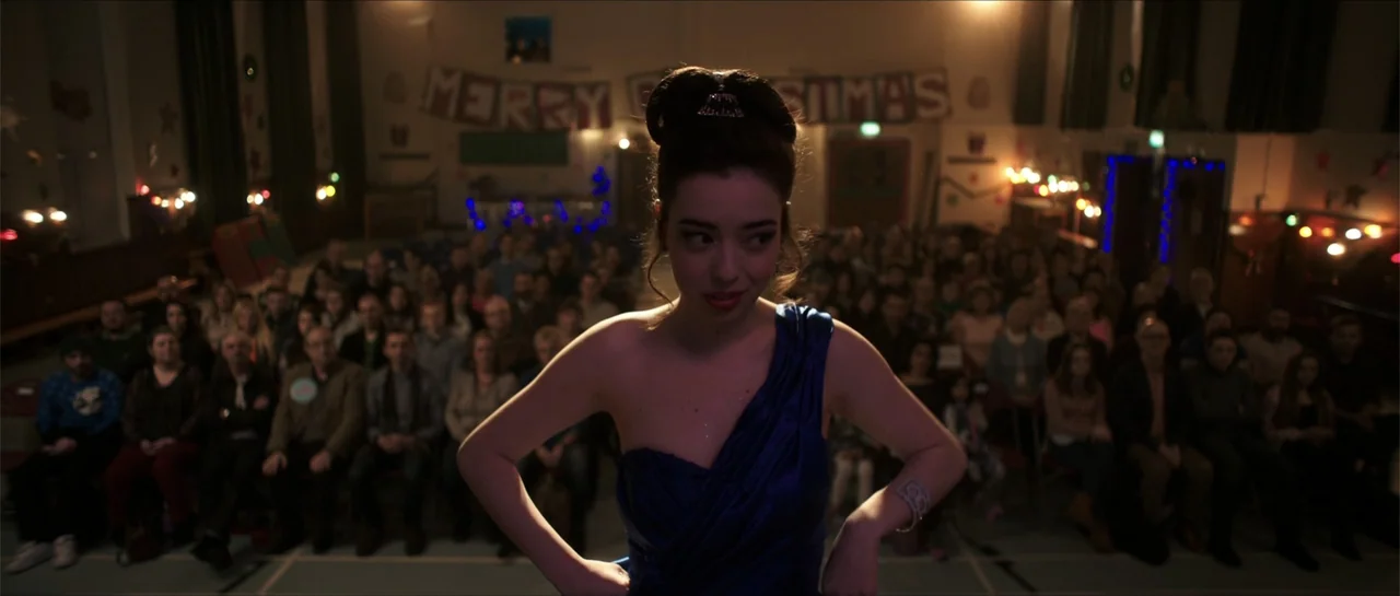 Anna and the Apocalypse (2018) movie still: medium — A community hall decorated with festive banners and string lights is filled with seated…