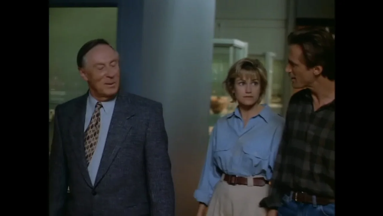 The Awakening (1995) movie still: medium — A museum hall features glass display cases in the background under soft lighting. Three people stand…