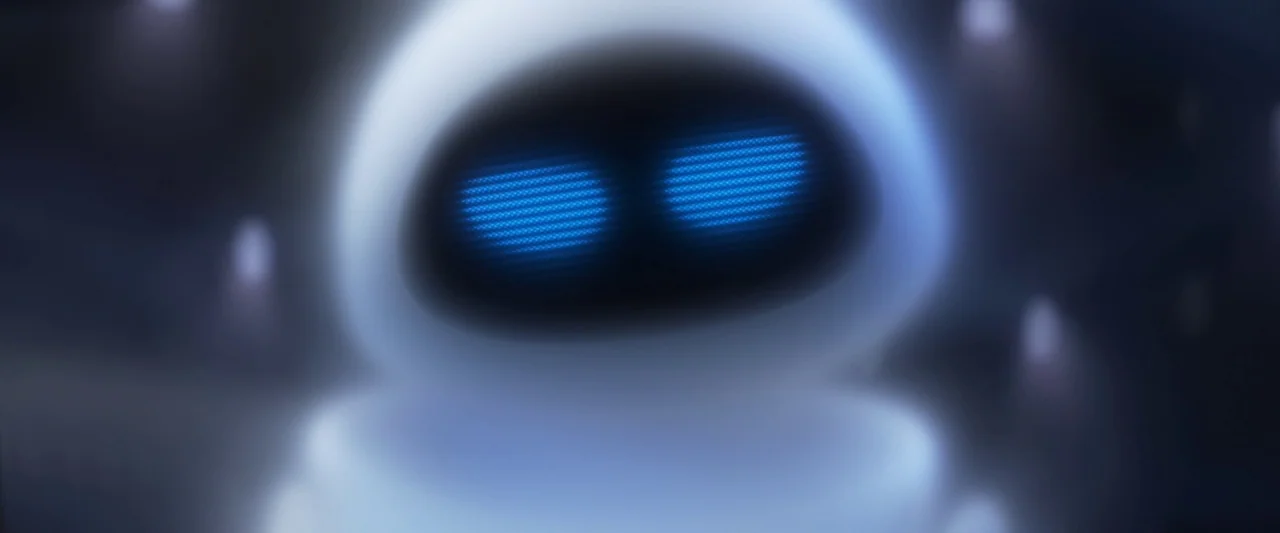 Wall-E (2008) movie still: closeup — A dark, blurred interior environment surrounds a glossy white robotic face. The robot displays glowing blue…