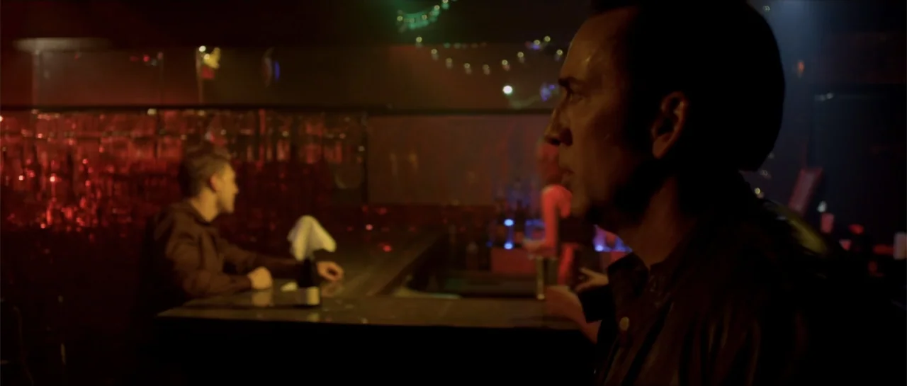 Rage (2014) movie still: medium — A dimly lit nightclub features a dark surface bar under red neon light. A man in a leather jacket stands near the…