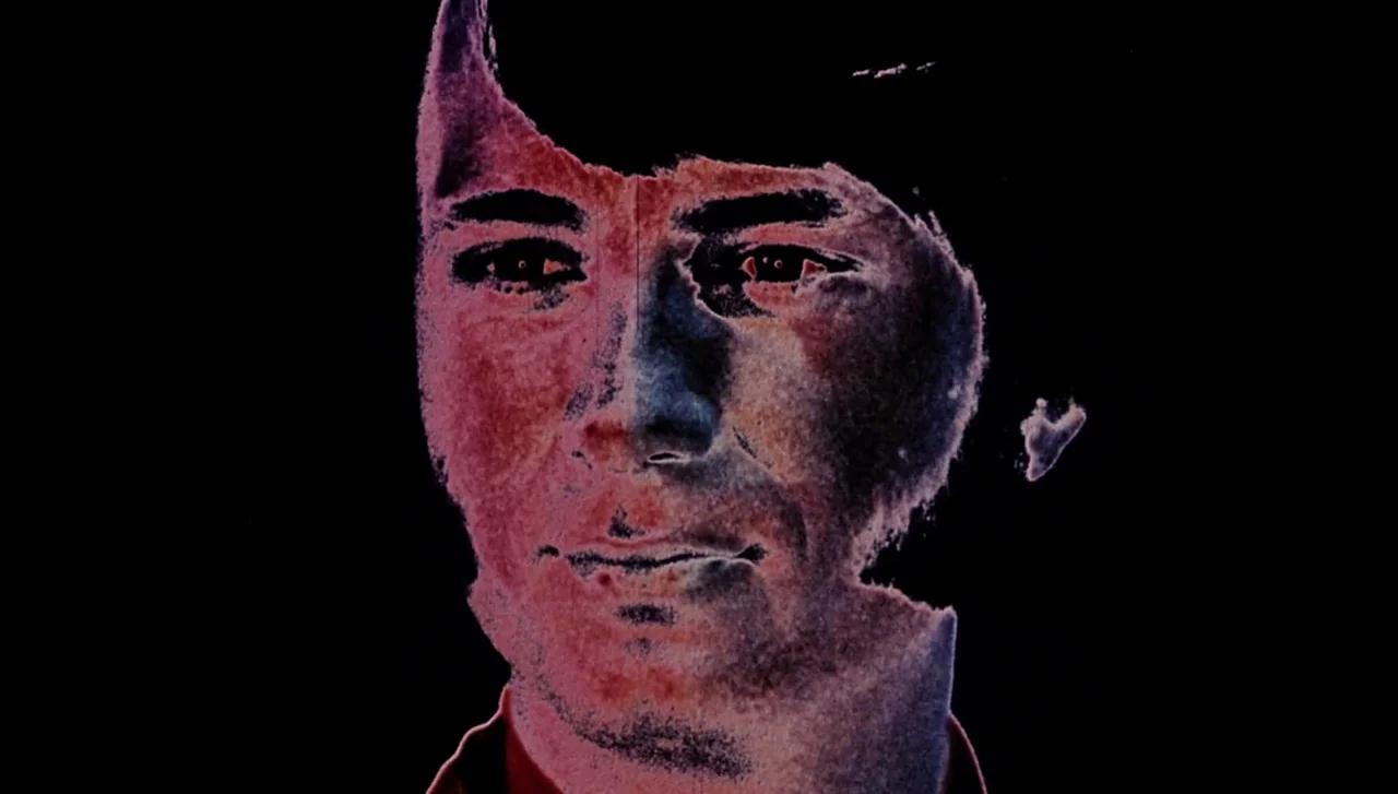 Head (1968) movie still: closeup — A dark abstract field surrounds a floating human face. The person stares forward with an inverted color treatment.