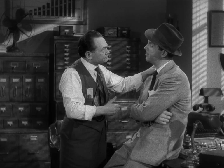 Double Indemnity (1944) movie still: medium — A vintage 1940s office features wooden file cabinets and a window with blinds. Two men stand in the…