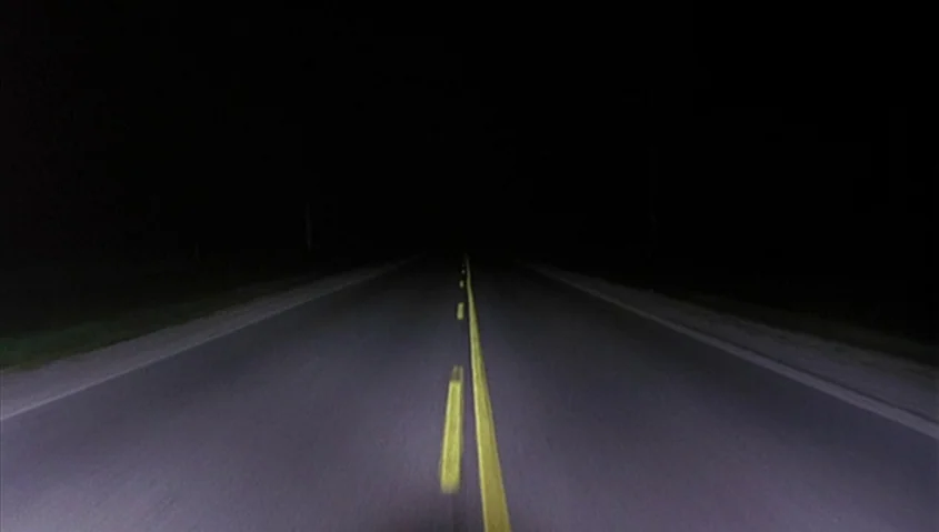 Dance Me Outside (1994) movie still: establishing — A dark, empty asphalt highway stretches into the distance at night. Yellow dashed lines run…