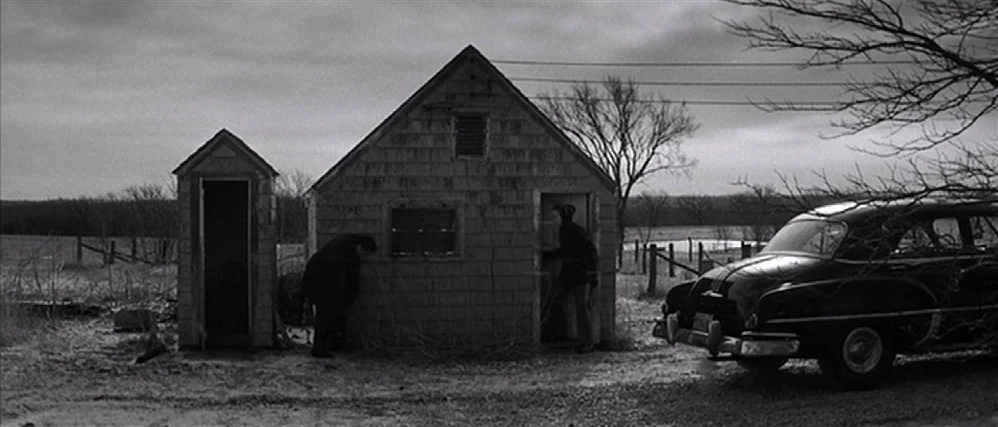 In Cold Blood (1967) movie still: wide — A rural setting with a small shingle-sided shed and an outhouse in a field. Two men stand by the building…