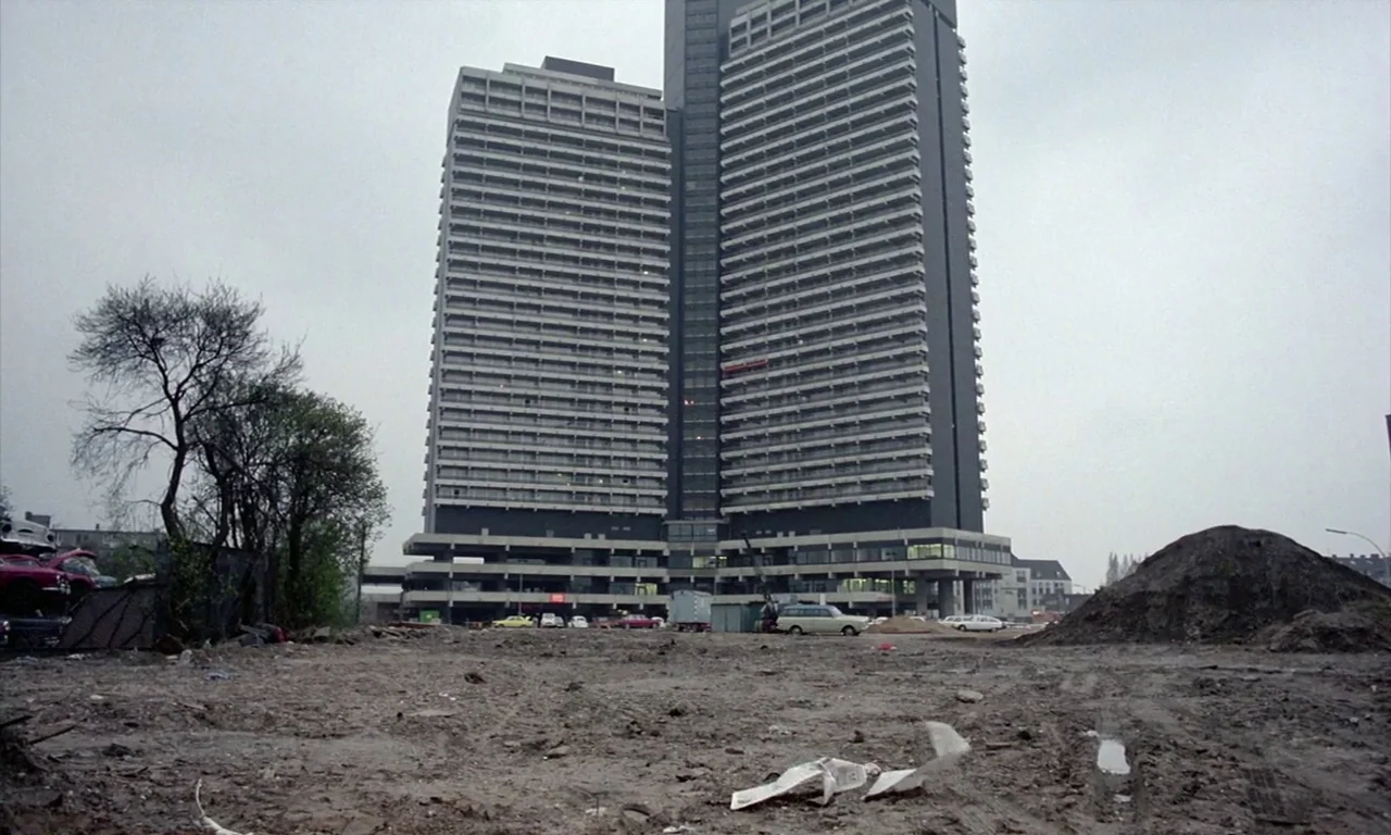 The Lost Honour of Katharina Blum (1975) movie still: establishing — A tall, monolithic brutalist building stands against a flat grey overcast sky.…