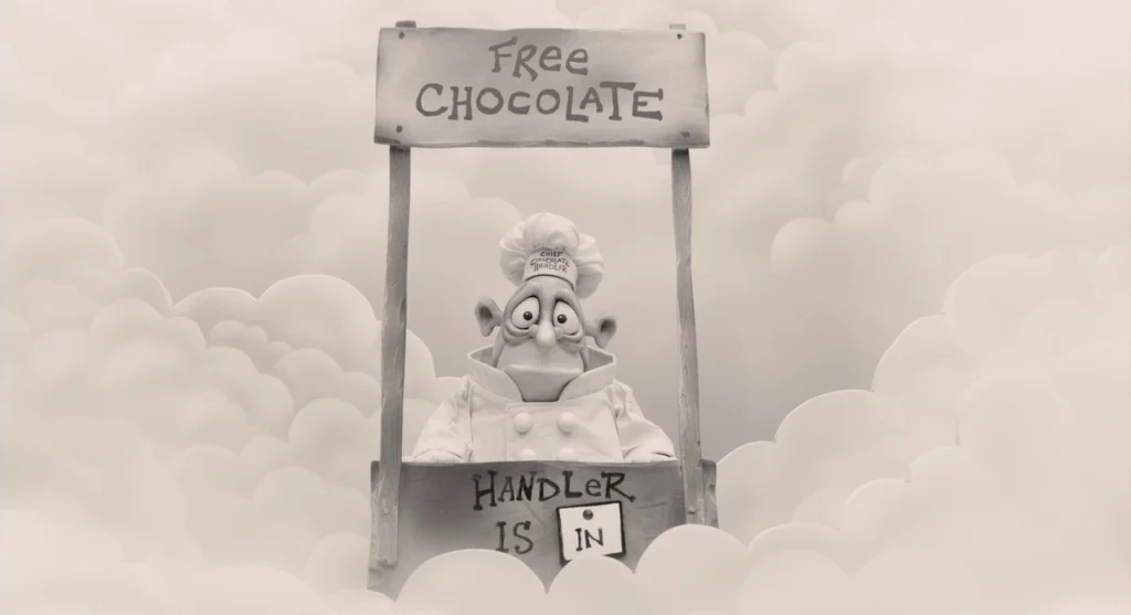 Mary & Max (2009) movie still: medium — A character stands behind a wooden booth against a backdrop of stylized paper clouds. The booth features a…