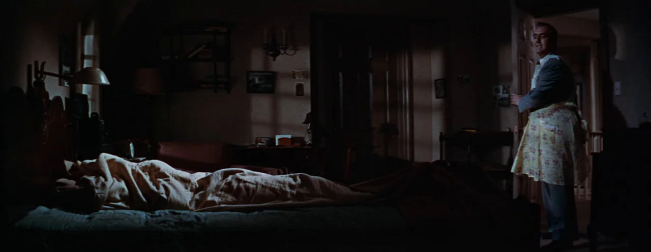 Rebel Without A Cause (1955) movie still: wide — A dark, sparsely furnished bedroom contains a bed occupied by a person under blankets. A…
