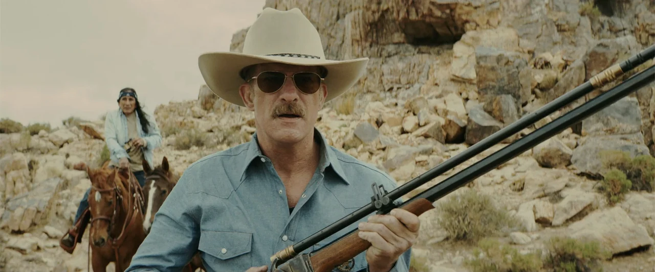 One Ranger (2023) movie still: medium — A rocky desert landscape with beige boulders and sparse dry shrubs serves as backdrop. A man in a cowboy hat…