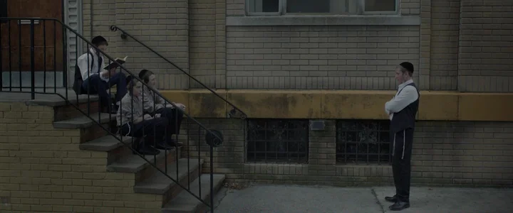 To Dust - Nightmares (2018) movie still: wide — A tan brick building with concrete stairs and barred basement windows at ground level. Three boys…