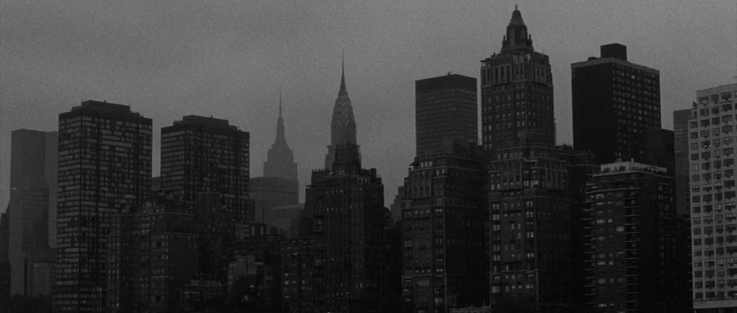 Manhattan (1979) movie still: establishing — A dense urban skyline features several high-rise apartment buildings under a dark, overcast sky. The…