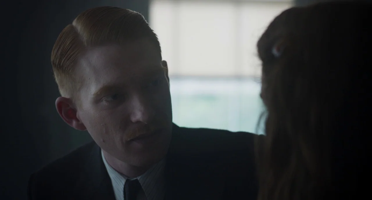The Little Stranger (2018) movie still: closeup — A man with red hair and a mustache leans in towards an unseen individual. The setting is a dimly…